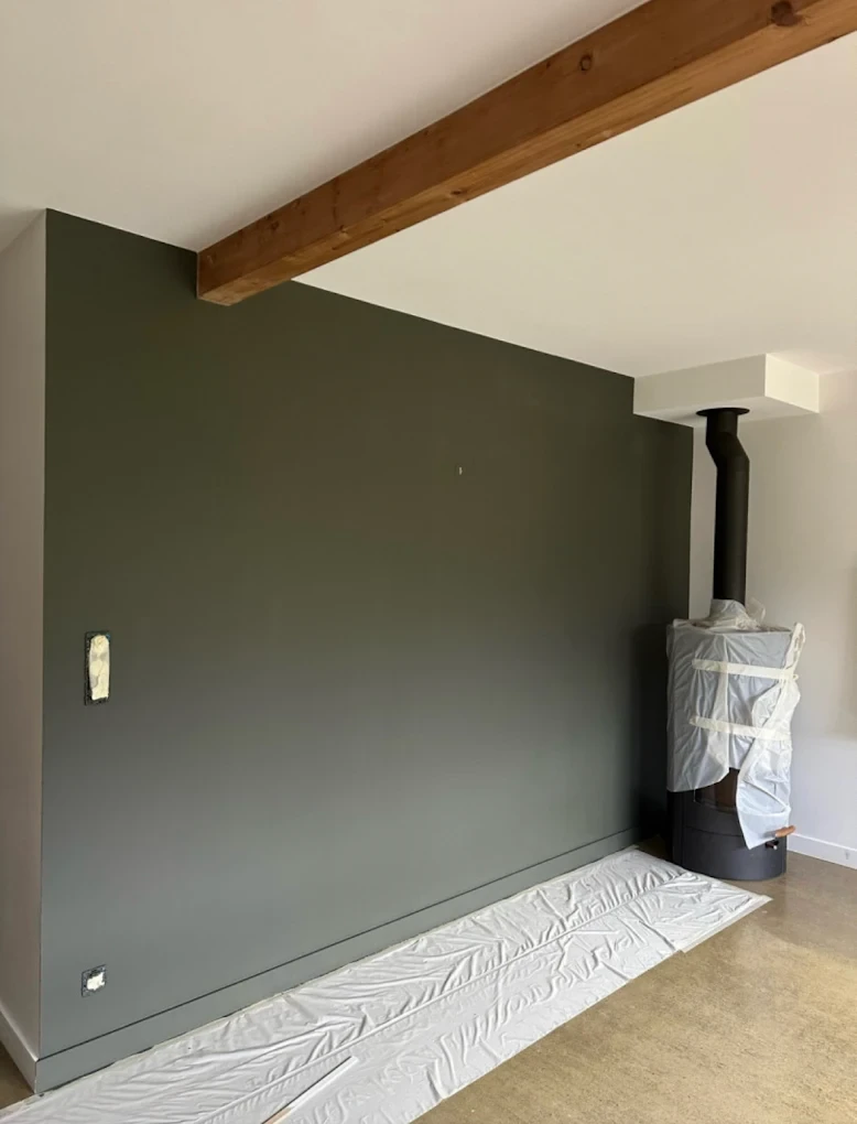 Mur intérieur peint en vert profond avec poutre en bois et poêle à bois